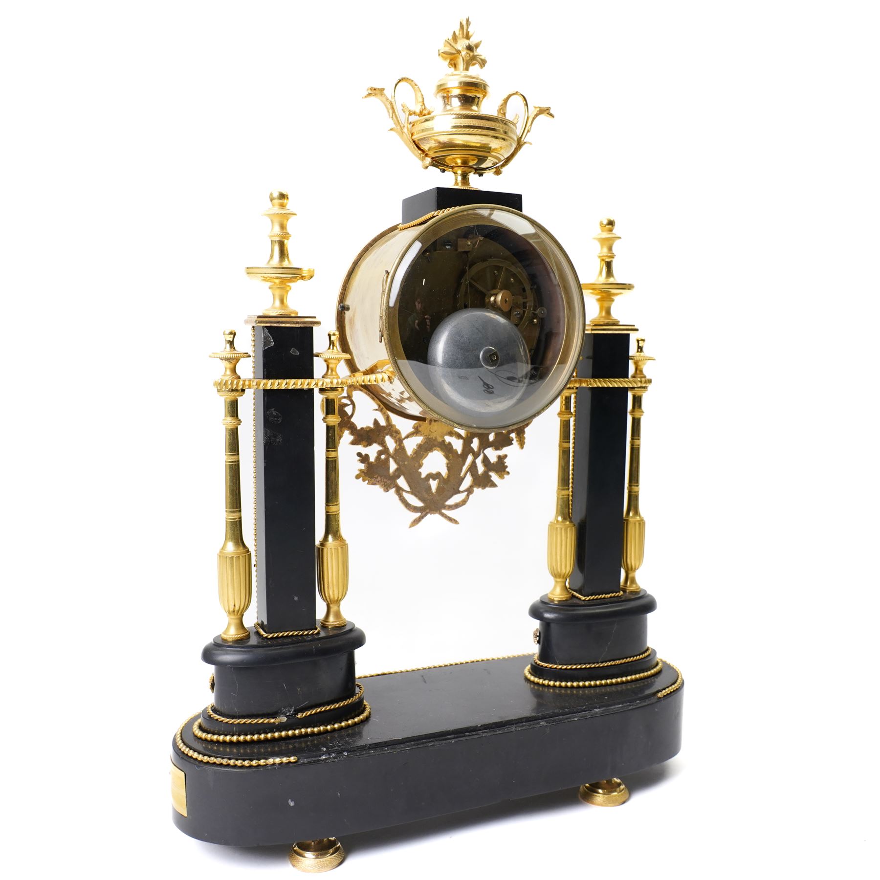 French-Early 19th century 8-day ormolu and polished black slate portico clock, case surmounted with a twin handled urn with flowers, supported by two square pedestals with finials and trailing floral mounts on oval bases, raised on an oval plinth with toupie feet, enamel dial signed 