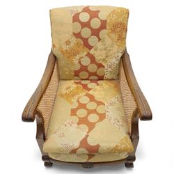 Pair of mid-20th century mahogany framed bergère armchairs, each with carved scroll arms and caned side panels, floral upholstered loose cushions, raised on cabriole front supports