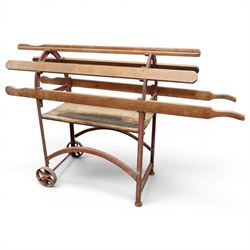 Cast iron and wooden saddle rack, arch form with shelf beneath and wheels to one end, pair...