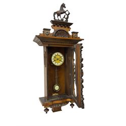 Victorian late 19th century German (HAC) 8-day striking wall clock striking the hours and half-hours on a coiled gong, in a walnut case with turned pilasters, pendant finials, applied carving and 'keyhole' door (glass missing), two-part dial with roman numerals and gothic hands, visible gridiron pendulum.