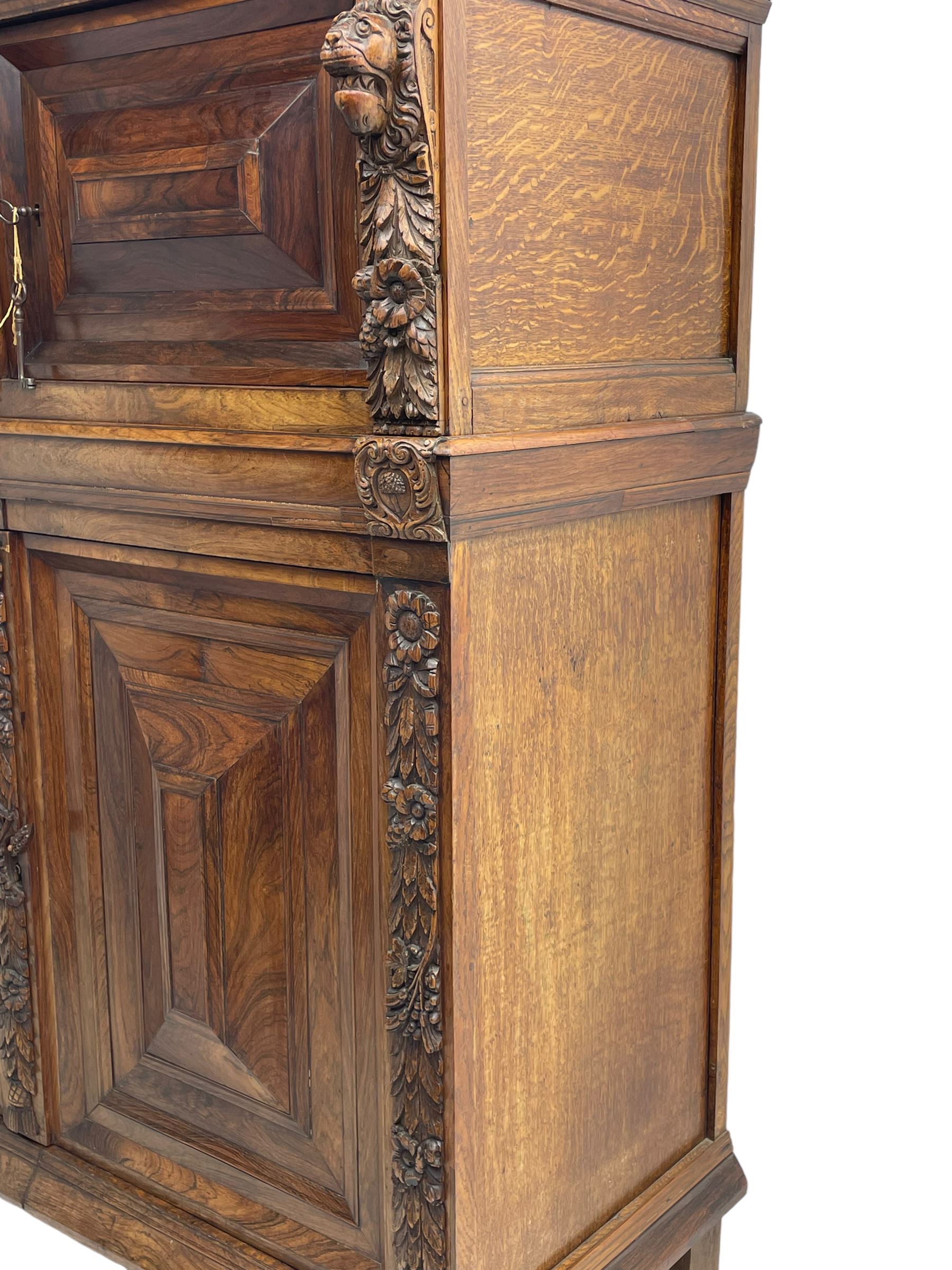 Late 17th century Flemish/Dutch rosewood and oak ‘Zeeuwse Kast’ or cupboard, projecting cornice carved with three putti masks, the uprights carved with lion masks over ribbons, flower heads and foliage, enclosed by four geometric panelled doors, lower central upright carved with flower head over foliate ribbon with bird among foliage, the escutcheon hidden by swivel berry carved cover, interior fitted with shelves, two drawers and shallow hinged cupboard, on two large turned and ebonised feet, circa 1680