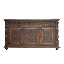Victorian heavily carved oak sideboard, the moulded top carved with foliate decoration to the edge, fitted with two drawers and three cupboards, the drawer fronts carved with green man mask handles and scrolling foliage, the panelled doors carved with interlacing foliage, on turned compressed bun feet