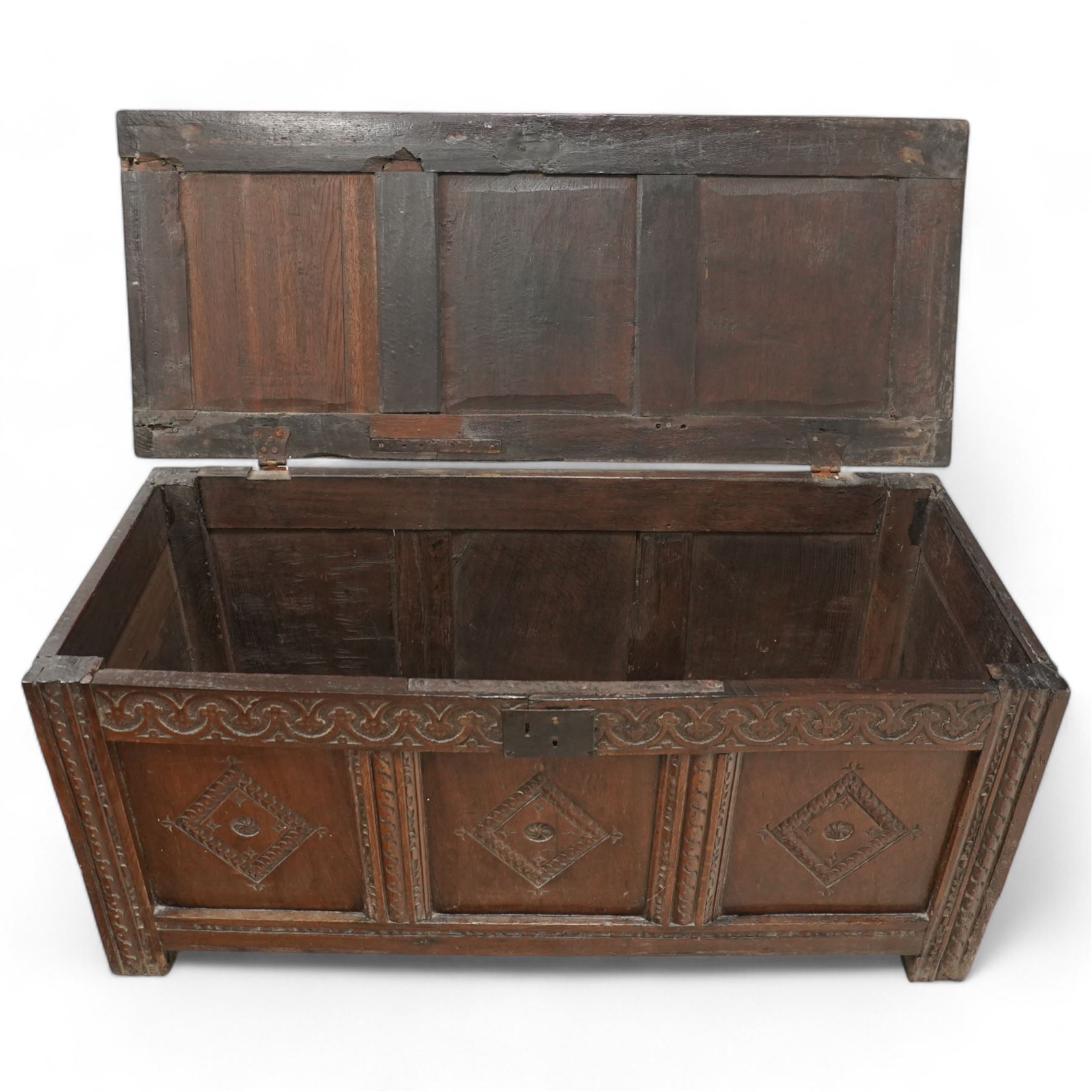 18th century oak coffer or blanket box, triple panel hinged lid over panelled front and sides, the front carved with scrolling foliate motifs and lozenges, moulded frame with chip carved decoration on stile supports 