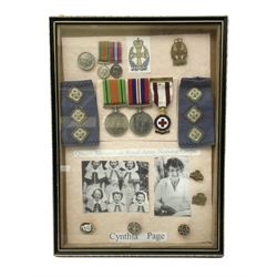 Framed display of medals and badges relating to Captain Cynthia Page of Queen Alexandra's Royal Army Nursing Corps including WW2 War Medal and Defence Medal with miniatures; Red Cross Society 3-Year Service Medal; Q.A.R.A.N.C. cap badge; Girl Guide and silver Scout badges; rank epaulettes; and related photographs 33 x 23cm