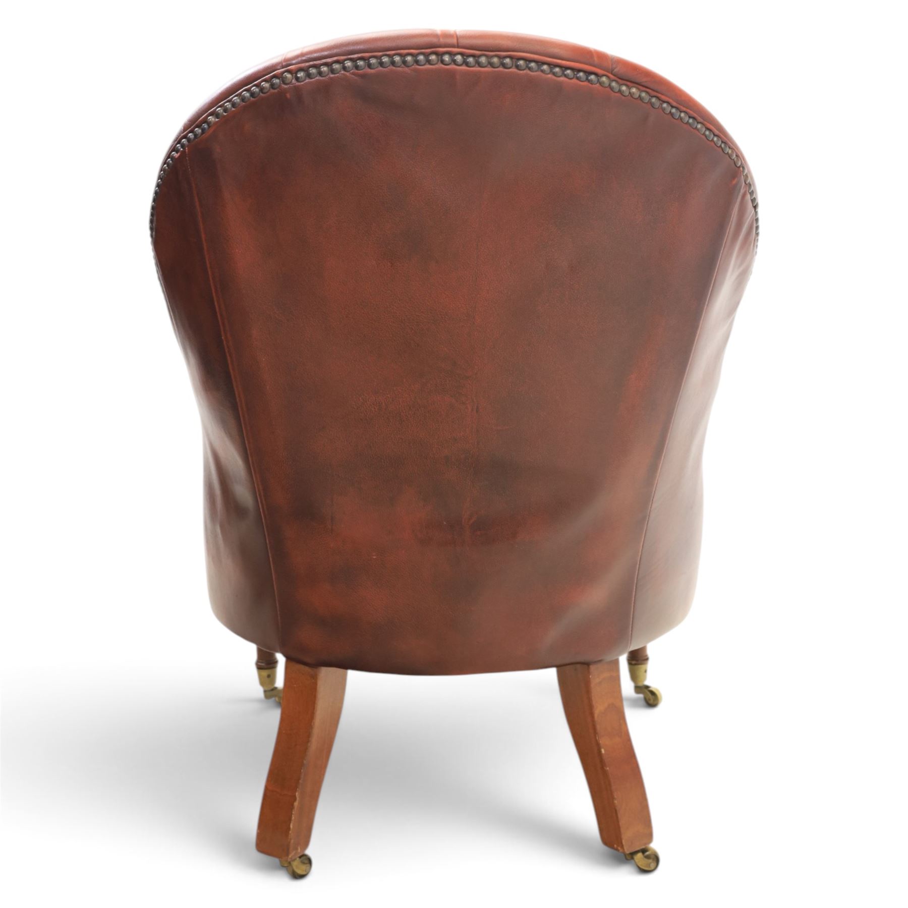 Victorian style oxblood leather armchair, deep button upholstered back and sides with rolled arms and brass studded borders, on turned front legs with brass and ceramic castors and splayed rear supports