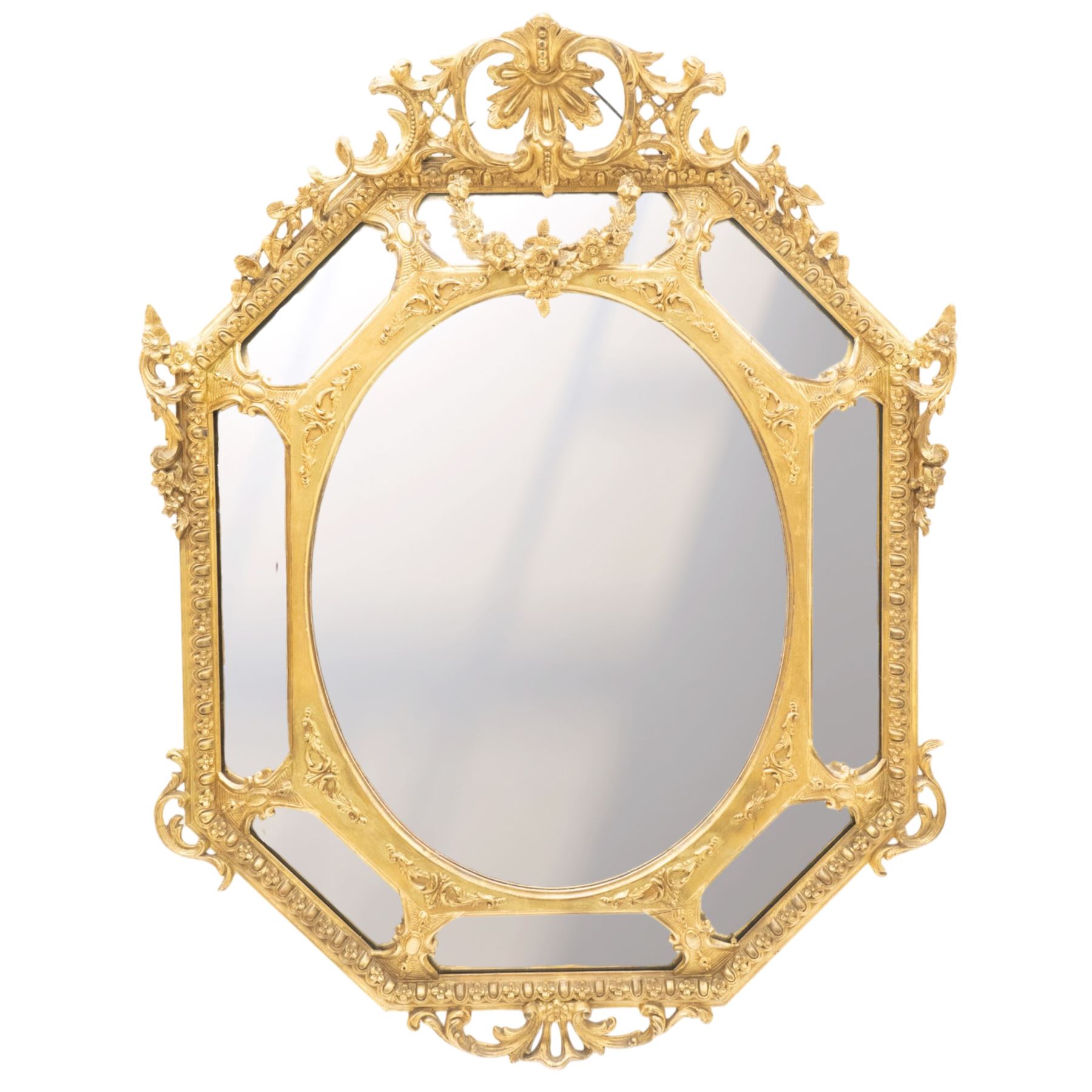 Late 19th century French giltwood and gesso wall hanging cushion mirror, the pierced foliate rocaille pediment extending acanthi C-scrolls and trailing bellflowers, over a floral garland and cartouche moulded rails, the central oval bevelled plate surrounded by further bevelled cushion mirrors, with out-scrolling pierced motifs flanking the floral egg-and-dart moulded outer edge, over a pierced foliate cartouche terminal