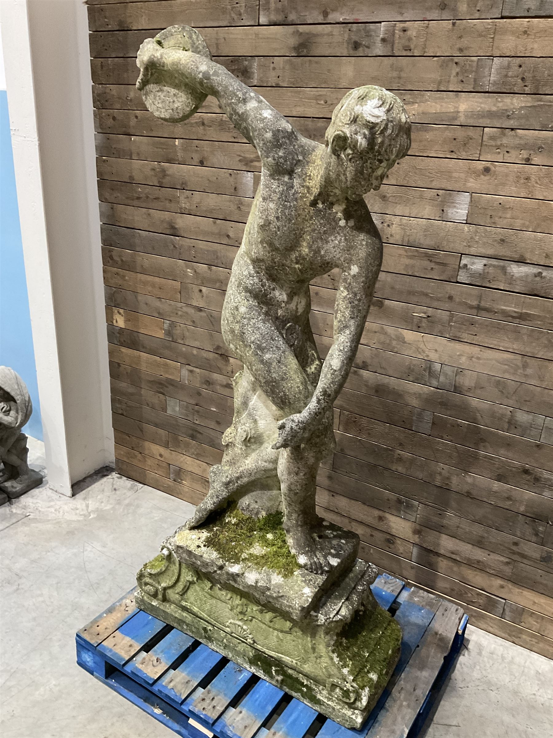 Life-size weathered cast stone Greek Discus Athlete, seated on rectangular slab raised on associated architectural plinth