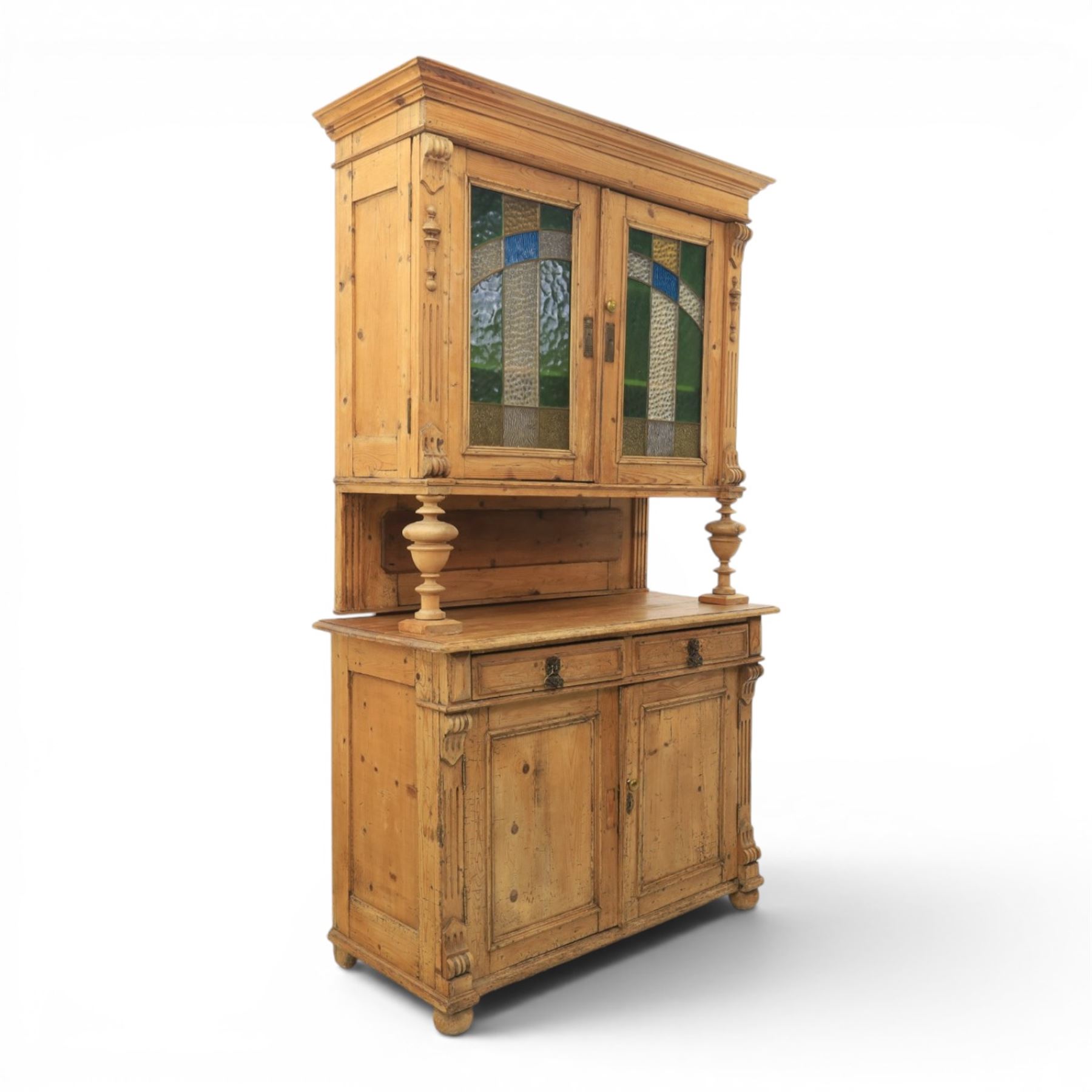 Late 19th century French pine dresser with stained glass upper section, the upper section with projecting cornice with fluted and scrolled details, enclosing a shelved interior, supported on turned front uprights, the lower section with frieze drawers and cupboard doors, raised on bun feet