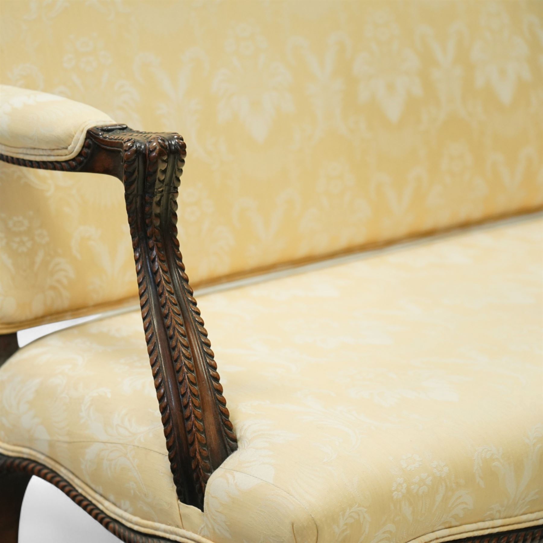 Early 20th century mahogany settee in the George III style, upholstered in pale yellow damask fabric, moulded serpentine seat rail with carved foliate detail, on cabriole supports with acanthus carved knees and scroll feet