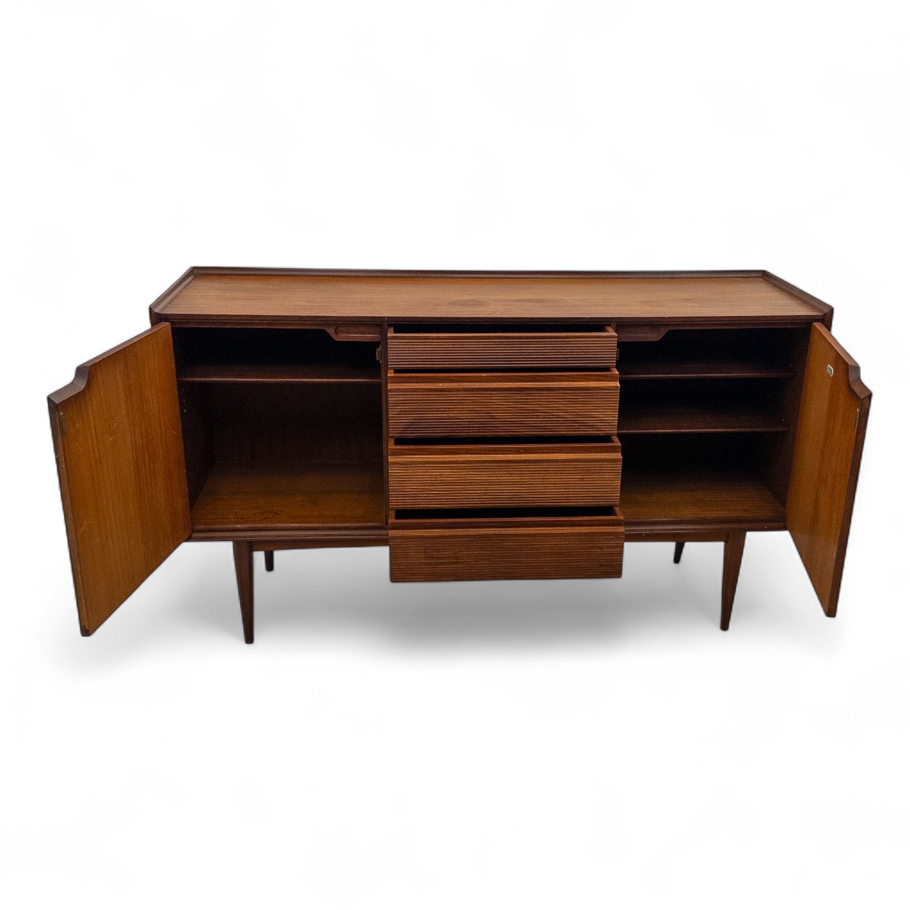 Richard Hornby for Fyne Ladye - mid-20th century afromosia teak sideboard, retailed by Heals of London, rectangular form, with low profile carved gallery lip, above three central drawers with ribbed drawer fronts, flanked by two cupboards with vertically grained doors and recessed pull handles, with streamlined moulded edges and sides, raised on tapered slender legs 