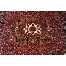 North West Persian Heriz/Ahar hand-knotted carpet, brick red field with a central bold stepped star medallion with pendants, surrounded by angular floral and geometric motifs, ivory spandrels, enclosed by a dark indigo border of stylized rosettes and vine motifs with multiple guard stripes, cotton fringe ends 