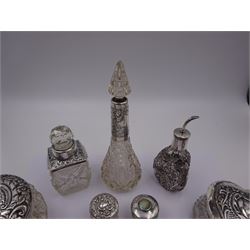 Two silver mounted dressing table jars, one in the form of a heart, both with embossed silver covers and cut glass bodies, hallmarked, together with two smaller examples, one set with mother of pearl, three silver mounted glass scent bottles, including an example with prunus blossom decoration, stamped Sterling, tallest bottle H17cm