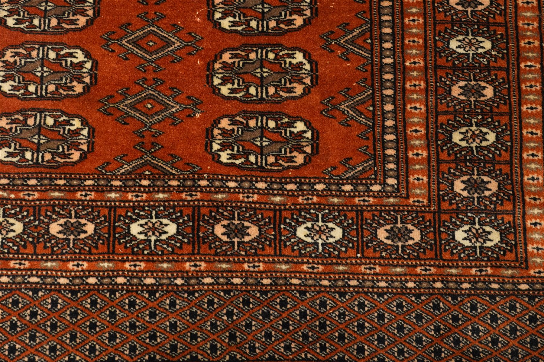 Bokhara hand-knotted carpet, terracotta ground with repeating rows of Tekke guls interspersed with geometric motifs, enclosed by multiple stylised floral and geometric borders, with fringed ends