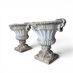 Pair of Neoclassical design cast stone garden urns, each of campana form with fluted body and gadrooned underbelly, decorated with faun/satyr opposing masks and ropetwist handles, with floral and mask design to the socles, raised on square bases, finished in weathered white patina