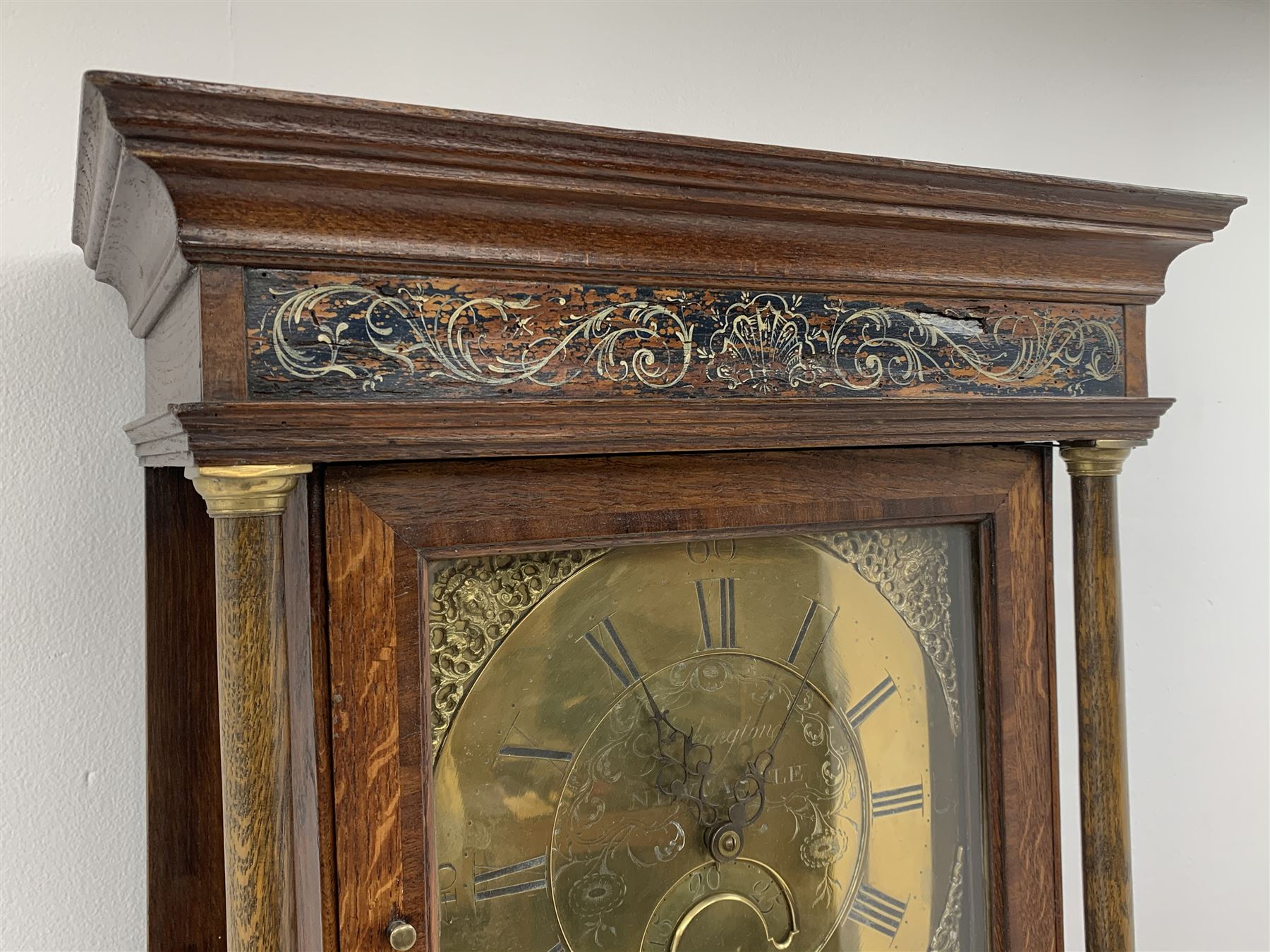 Early 19th century oak longcase clock, projecting cornice over frieze painted with scrolls, square glazed door enclosed by plain pilasters, square brass dial with ornate cast metal spandrels, Roman chapter ring and false subsidiary date aperture, engraved decoration and inscribed 'Torkington, Newcastle', 30-hour movement striking on bell