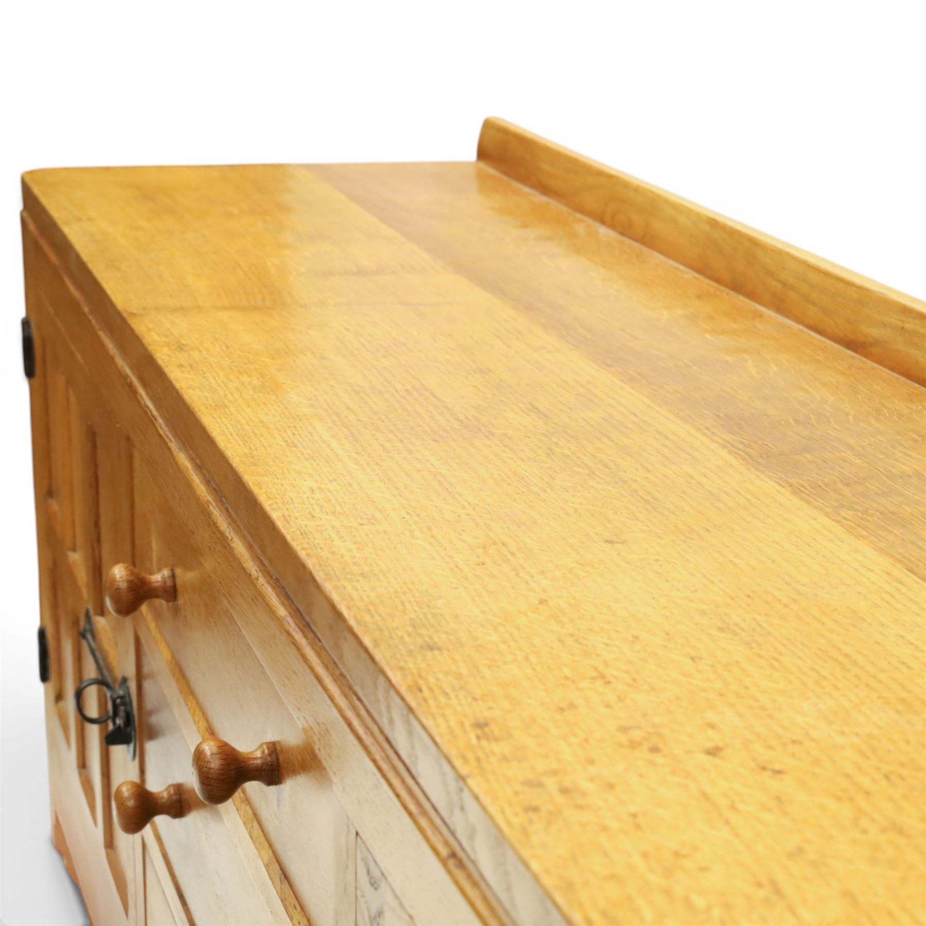 Mouseman - large adzed light oak sideboard, the rectangular top with raised galleried back, fitted with three central drawers flanked by panelled cupboards enclosing shelves, with wrought iron fittings, raised on octagonal feet, with signature carved mouse, by the workshop of Robert Thompson, Kilburn