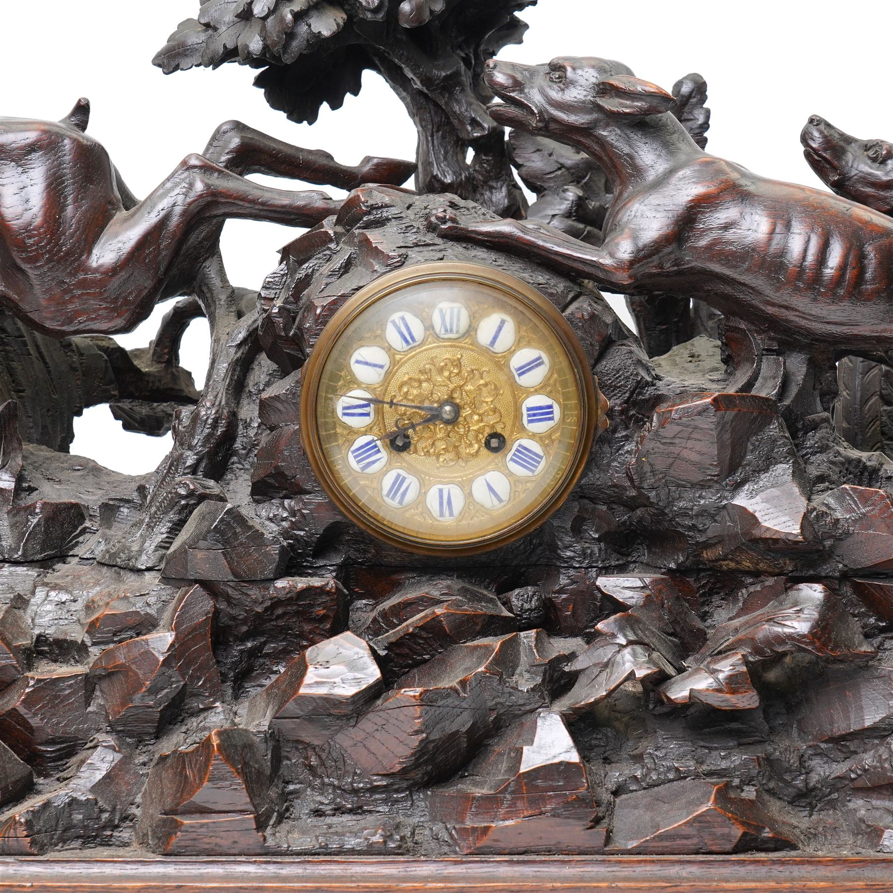 19th-century-8-day German Black Forest mantel clock c1880, with a carved oak case depicting a hunting scene with a stag pursued by hounds amidst rockwork and oak foliage, fitted with a French Parisian movement with a cast brass dial enclosed within a glazed brass bezel with a pendulum adjustment arbor, cartouche blue-on-white enamel  Roman numerals, engraved five minute Arabic's and contrasting steel Fleur-di-Lis hands, twin train going barrel movement with a recoil anchor escapement and countwheel strike. With pendulum.  