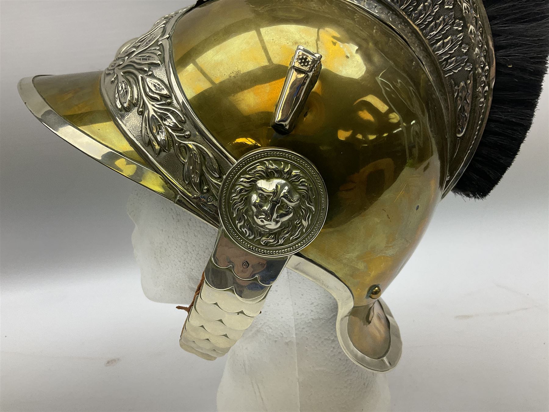 Early 20th century French mounted gendarme's helmet, brass with nickel-silver mountings, broad band embossed with fused grenade, high comb with the face of the gorgon Medusa at the peak and with a black horse hair crest, plume socket at the left, leather-backed nickel-silver chin scales with lion mask mounts.