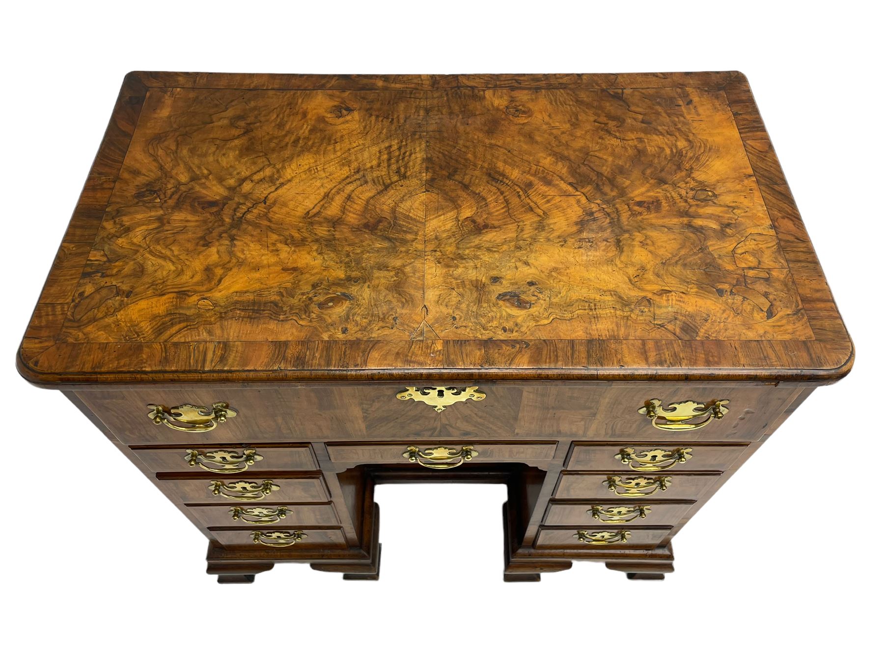 Early 18th century Queen Anne figured walnut kneehole desk with secretaire drawer, moulded and book matched top with walnut band, the top drawer with fall front enclosing small drawers and pigeon holes, fitted with nine drawers and central recessed cupboard, on ogee bracket feet