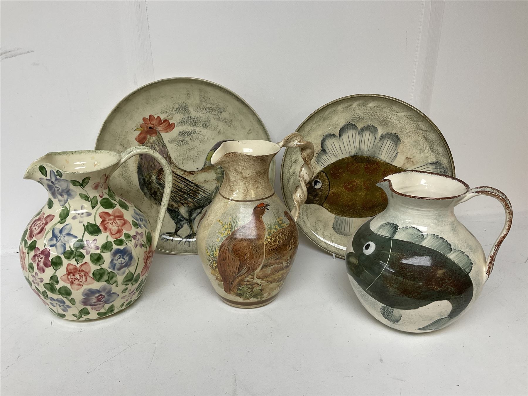 Collection of Yorkshire Moorlands Pottery, comprising two large circular dishes and three jugs, decorated with various fish, flowers, red grouse and cockerel