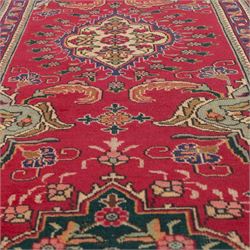 North West Persian Tabriz hand-knotted runner, madder red field with central octagonal medallions of sage green, navy and ivory, ground enclosing a floral rosette and radiating angular vinery, scrolling floral sprays and palmettes either end with shaped pendants principal border on navy ground decorated with a continuous vine-scroll of palmettes and rosettes, flanked by narrow guard borders, with cotton fringe ends 