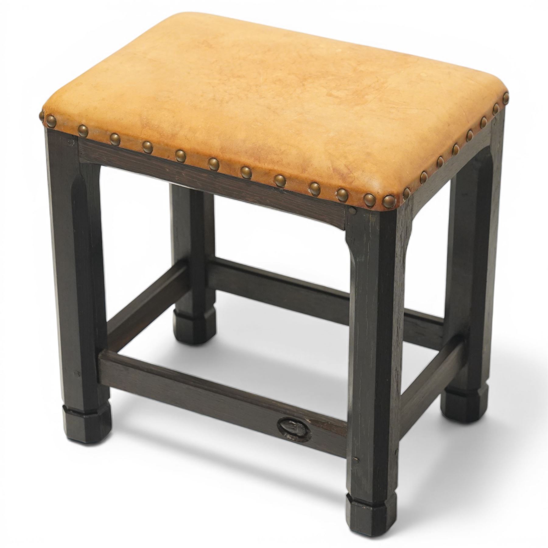 Acornman - dark stained oak stool with upholstered seat, rectangular top with tan leather seat with studded trim, raised on octagonal supports, with carved acorn signature, by the workshop of Alan Grainger of Brandsby