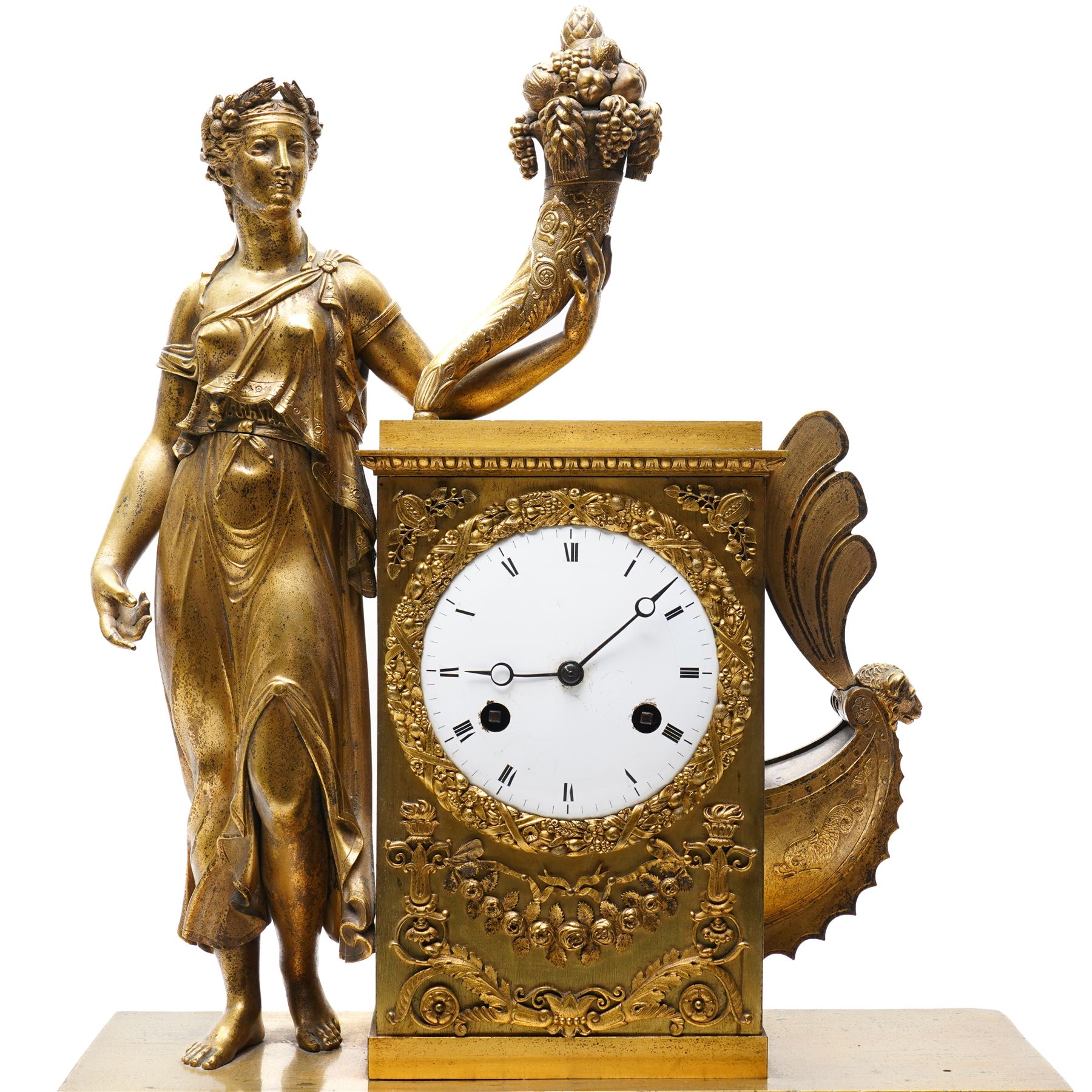 Empire period-gilt brass early 19th century French figural mantel clock c1820, the case surmounted with a figure of Ceres the Roman goddess of plenty holding a cornucopia overflowing with fruit and corn, supported on a rectangular plinth base with depictions of putti representing the arts and labour, movement case with floral garlands and a leaf and ribbon dial bezel, convex white enamel dial with moon hands and short Roman numerals, with a  Parisian 8-day twin-train countwheel striking movement and silk suspension, striking the hours and half-hours on a bell.
With pendulum and key. 
