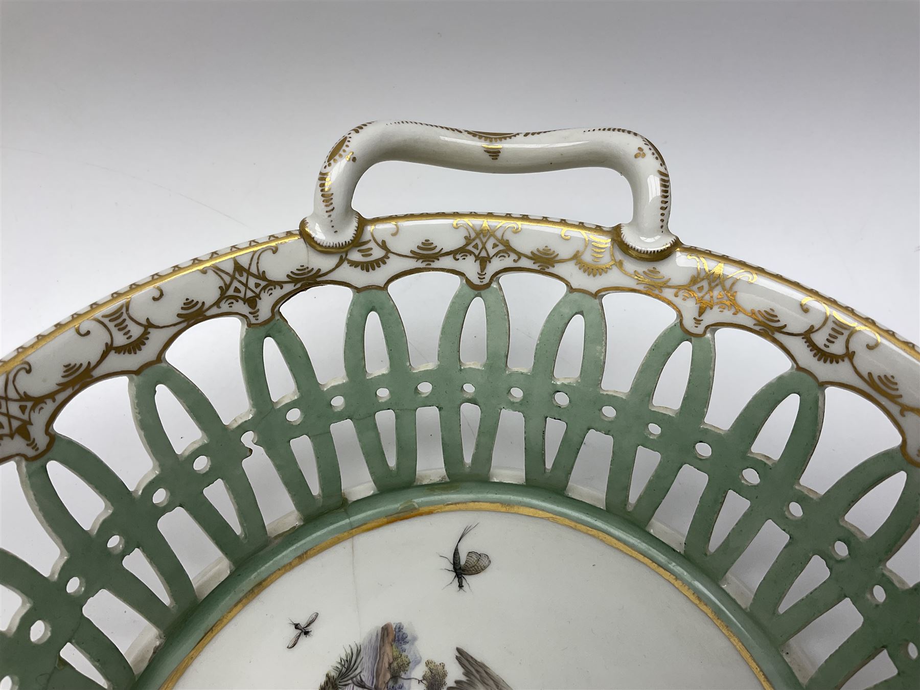 Pair of 19th century German openwork chestnut baskets, with twin handles and scrolling gilt border and star rim, painted to the centre with birds and insects, D22cm 