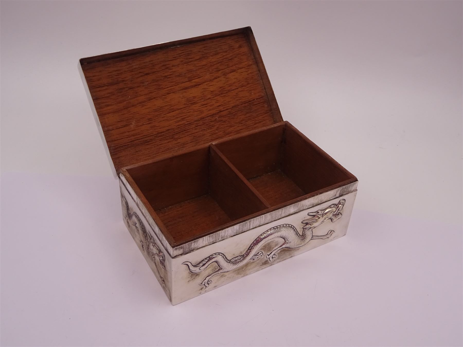 Late 19th century/early 20th century Chinese export silver mounted cigarette box, of rectangular form, decorated in relief with dragons, the hinged cover with similar dragon decoration and central blank oval cartouche, opening to reveal a softwood lined compartmentalised interior, stamped beneath with character mark and KMS for maker Kwong Man Shing, H6.3cm, W15.5cm, D9.5cm