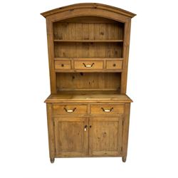 Pine farmhouse style dresser, arched top with projecting cornice over two tier plate rack and three small drawers, base fitted with two drawers with ceramic handles and two panelled cupboards, on turned feet
