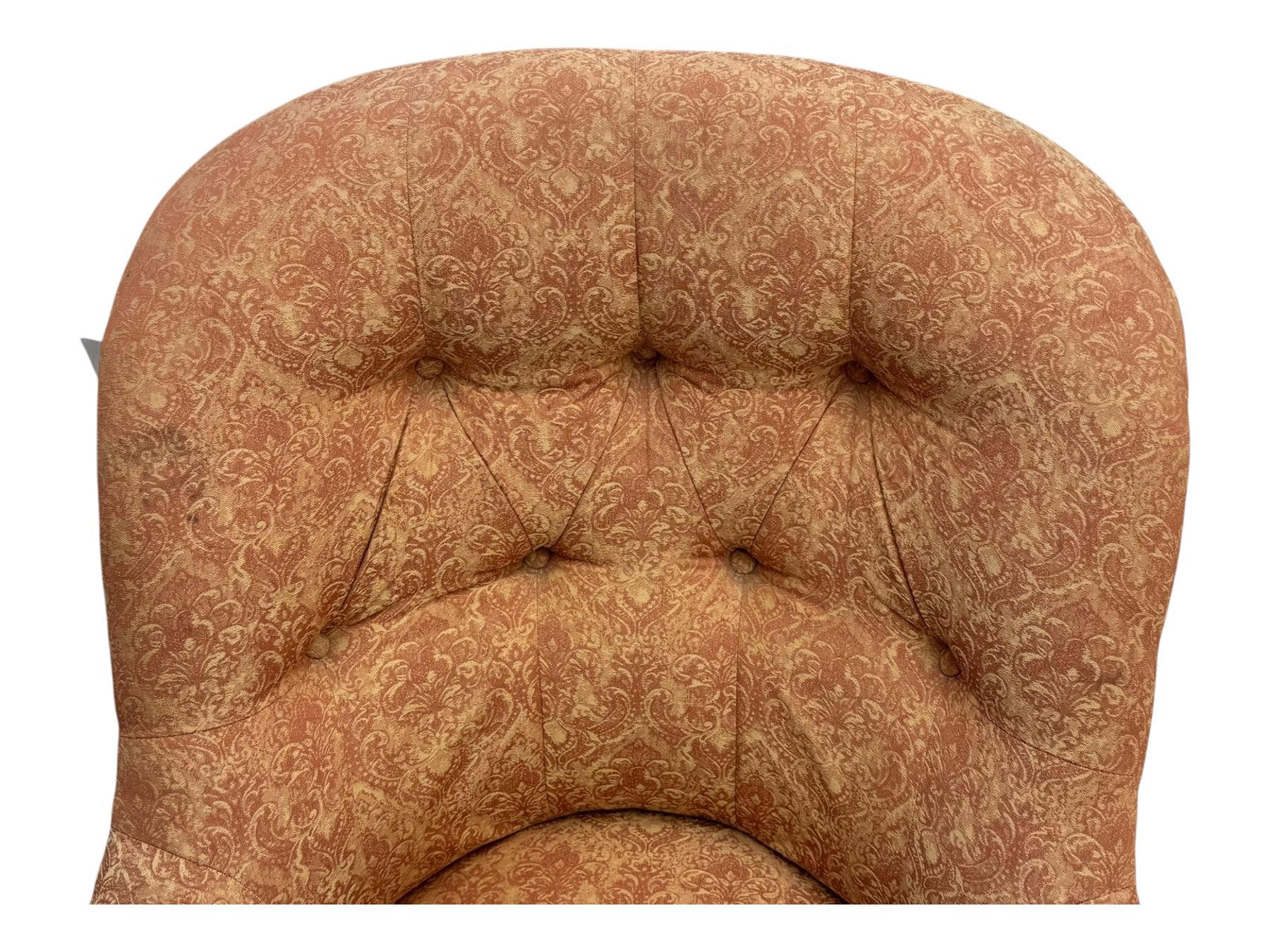 Late Victorian nursing chair, of tub form with deep buttoned backrest, upholstered in pink damask fabric with foliate motifs, raised on turned mahogany legs with brass caps