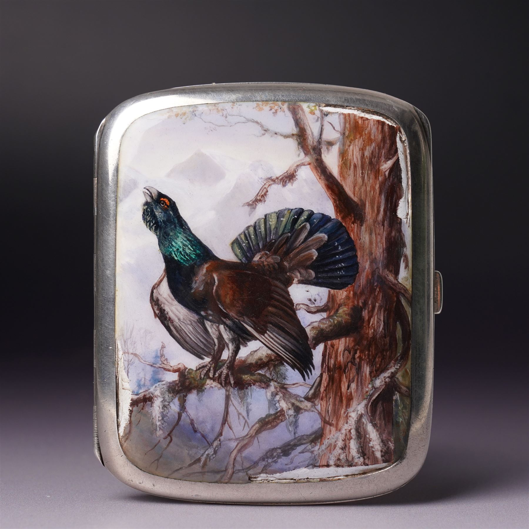Early 20th century Continental silver and enamel cigarette case of rectangular cushion form, the front enamelled with a capercaillie in a Scottish woodland scene, marked 935, 9cm in length