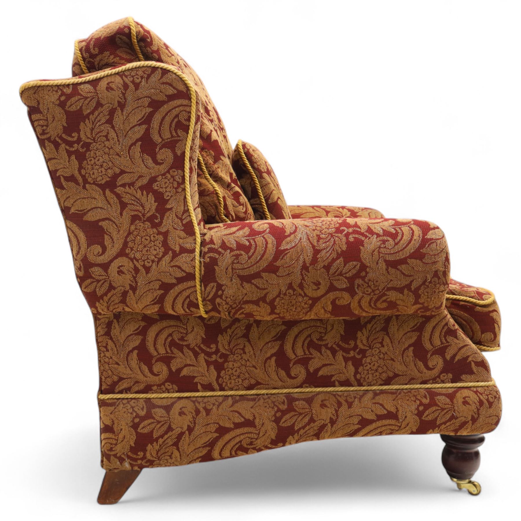 Duresta – pair of armchairs, upholstered in red and gold damask fabric with piped edges, scroll arms and loose feather-filled cushions, raised on turned wooden feet with brass castors