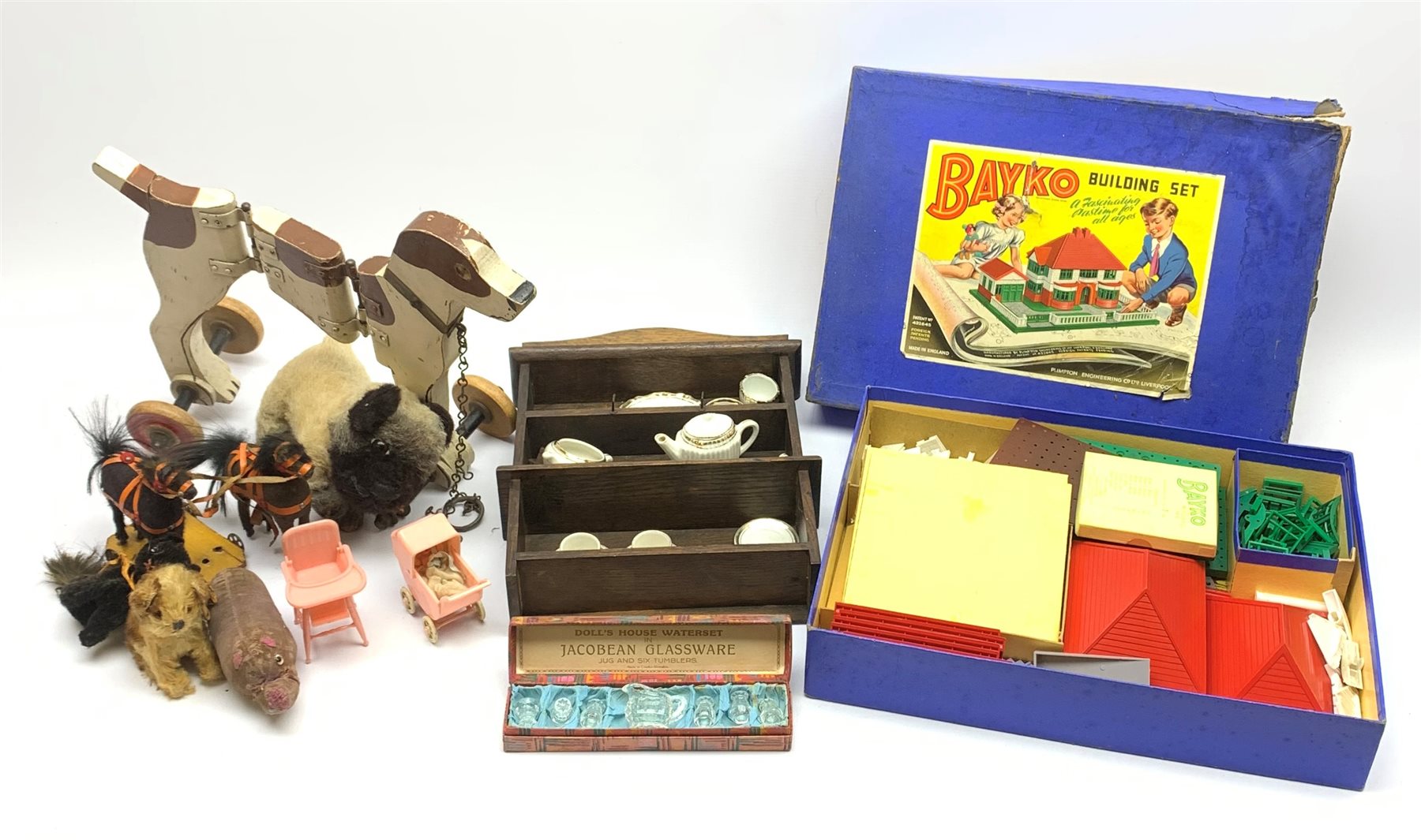 Bayko Building Set No.2, boxed; doll's wooden Welsh dresser with thirteen pieces of white/gilt porcelain tea and dinnerware, boxed seven piece glass waterset and Kleeware miniature baby's high chair and pram; articulated wooden pull-along dog; small pull-along toy of two horses; and four various soft toys