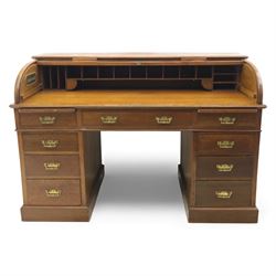 Edwardian oak roll-top desk, the tambour enclosing a fitted interior of pigeonholes and dividers, over a central kneehole flanked by twin banks of drawers with brass handles, on plinth bases