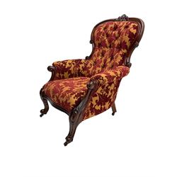 Late 19th century mahogany framed spoonback armchair, cresting rail carved with central cartouche, the scrolled arm terminals supported by foliate carved supports terminating in castors, upholstered in deep red and orange foliate patterned fabric with sprung seat