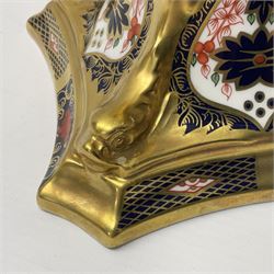 Pair of modern Royal Crown Derby Old Imari 1128 pattern candlesticks, each with shaped drip tray affixed to squat socket, upon spreading stem and canted square base with gilt dolphin edges, with printed marks beneath including Roman numeral year cypher for 2003, H26.5cm, with original boxes