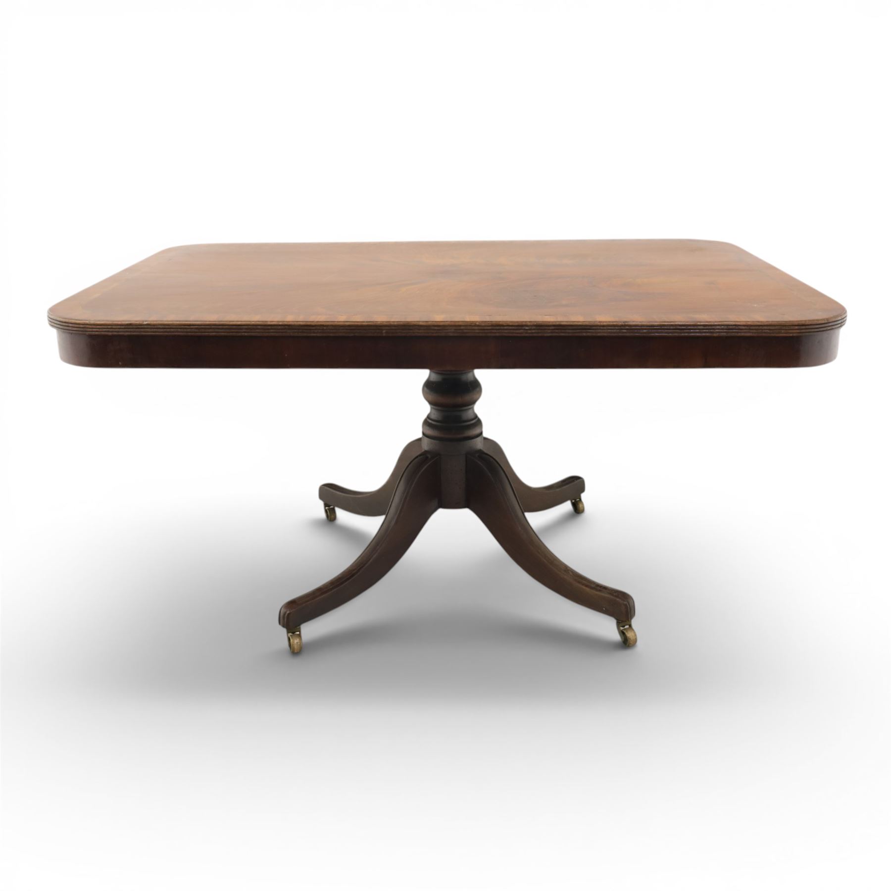 Regency mahogany tilt-top dining table, crossbanded rounded rectangular top, raised on a splayed base, terminating in brass castors