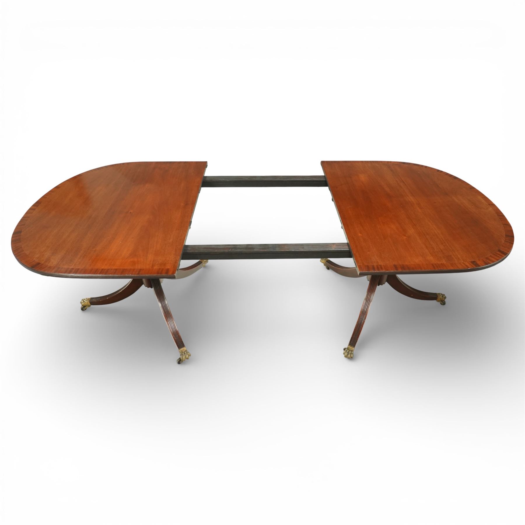 Arthur Brett & Sons - Regency design mahogany extending dining table and eight chairs, the oval top with rounded ends and two extension leaves, raised on twin pedestal supports with swept legs terminating in brass caps and castors, accompanied by a set of eight chairs comprising six single chairs and a pair of carvers, the chairs with curved backs and horizontal splat rails, upholstered seats, sabre legs and scrolling arms to the carvers
(Extends to 252cm)
(Chairs H 86cm, W 52cm)