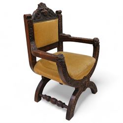 Victorian heavily carved oak X-framed throne chair, the cresting rail carved with mask and curling foliage, upholstered in mustard fabric, the arms and frame carved with scrolling foliage, united by turned stretchers 