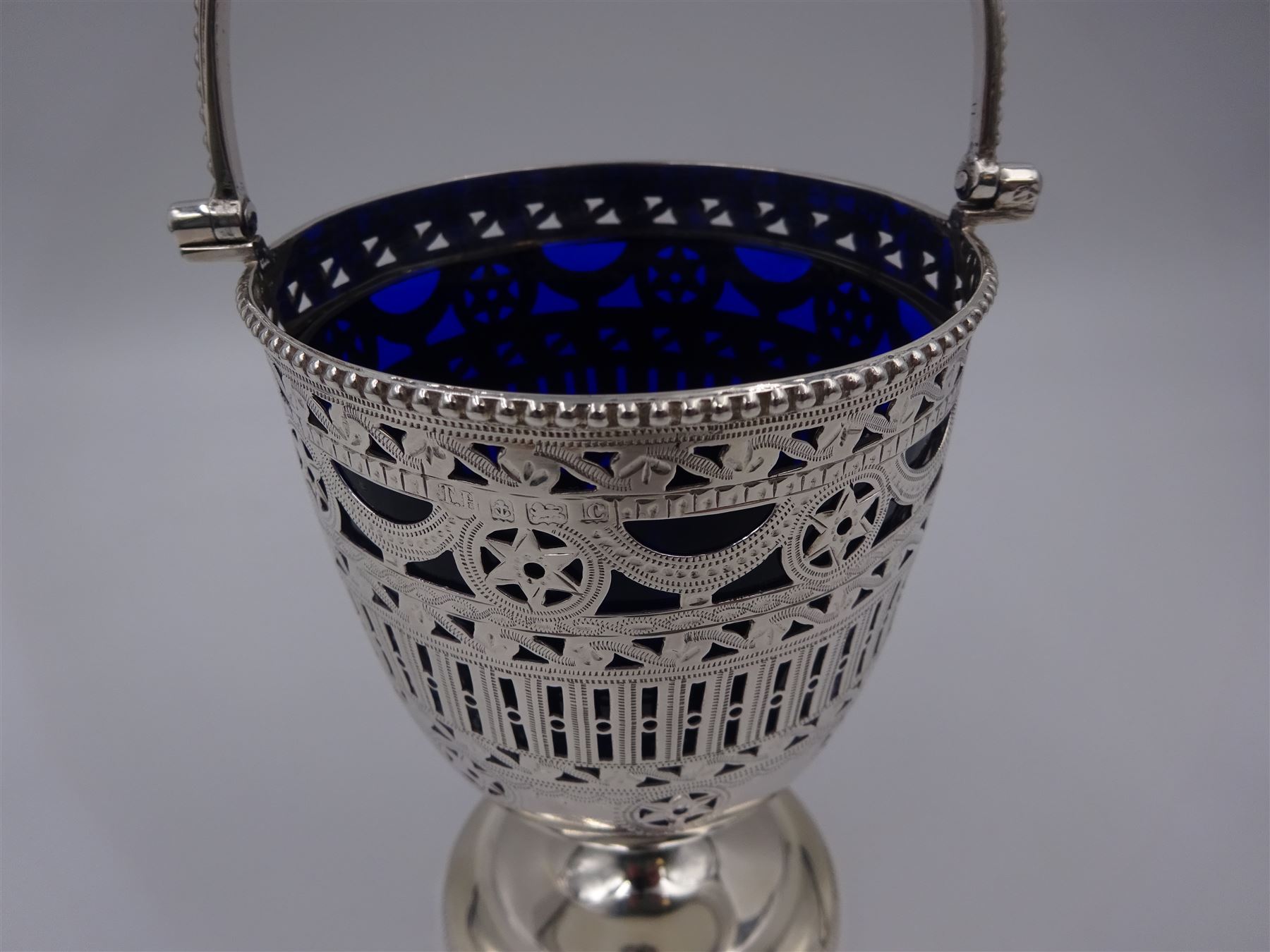 Edwardian silver swing handled sugar basket, with pierced and engraved star and foliate decoration to body, with beaded rim and handle, upon stepped circular base, hallmarked Thomas Hayes, Birmingham 1902, not including handle H10.8cm, with blue glass liner