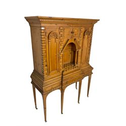 20th century pine architectural collector's cabinet on stand, projecting dentil cornice over various compartments, central recessed arch with turned pillar supports and sloped arch pediment, fitted with four cupboards, false brickwork uprights to front and corners, central hidden drawer revealing cube work surface, lower moulded plinth, the stand with foliate carved mouldings, on six square tapering supports with brass castors