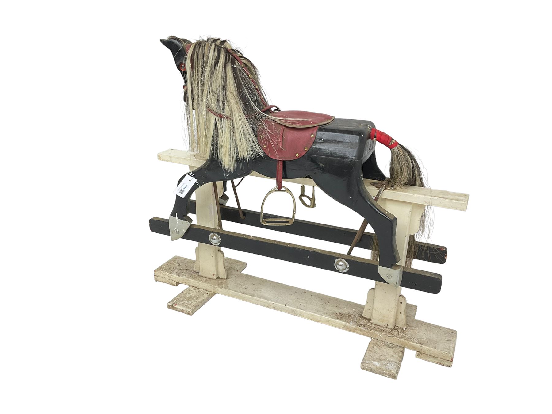 20th century black painted rocking horse on white painted trestle base, fitted with saddle and stirrups 