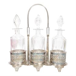 Late 19th century silver plated Silber & Fleming triple decanter stand, the three cut glass decanters with spire stoppers housed within foliate and scroll pierced bottle sleeves, upon a tripart base with six scroll feet, the base mounted with articulated x-frame curved handle, including handle when positioned upright H35.5cm, W34cm