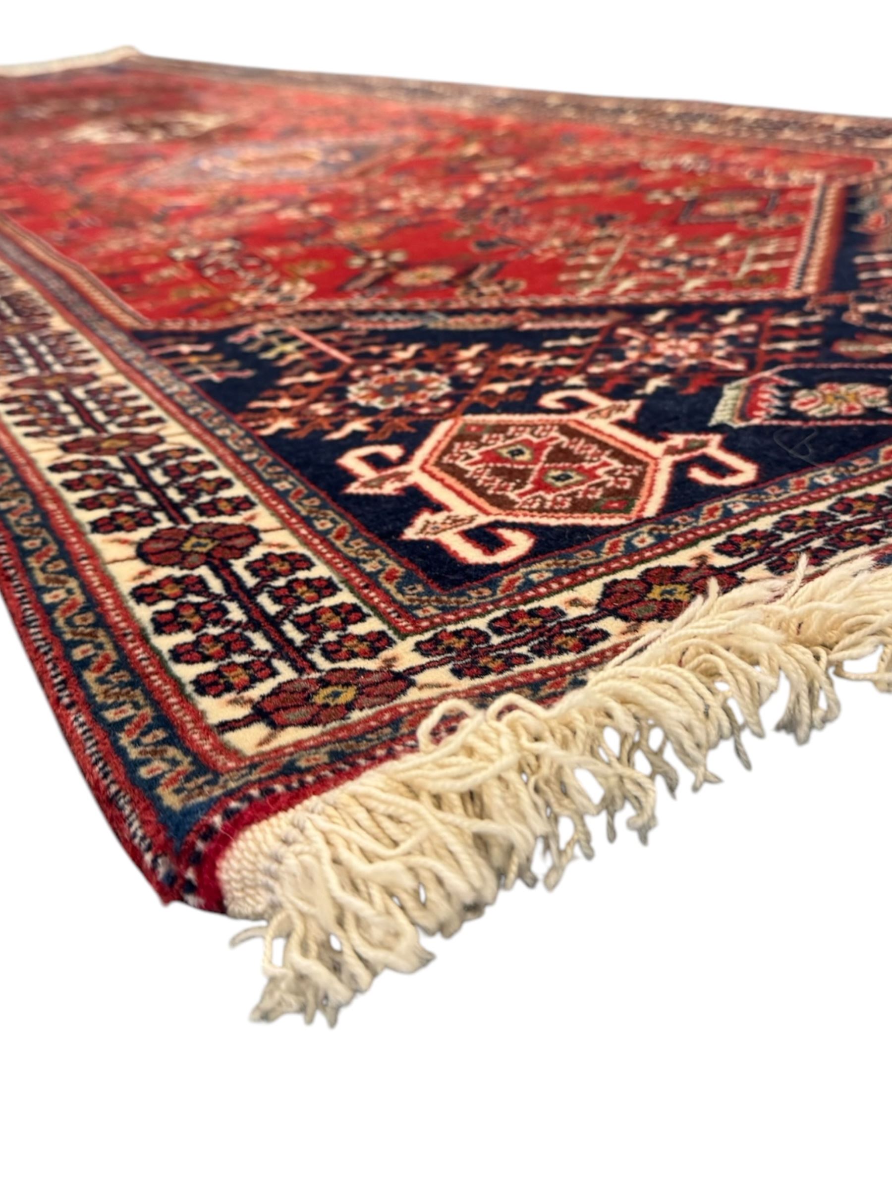 Persian Qashqai crimson ground runner, the central field decorated with three large geometric medallions with intricate angular and floral motifs, the indigo spandrels with complementary geometric designs, bordered by an ivory band with repeating floral patterns and angular vines