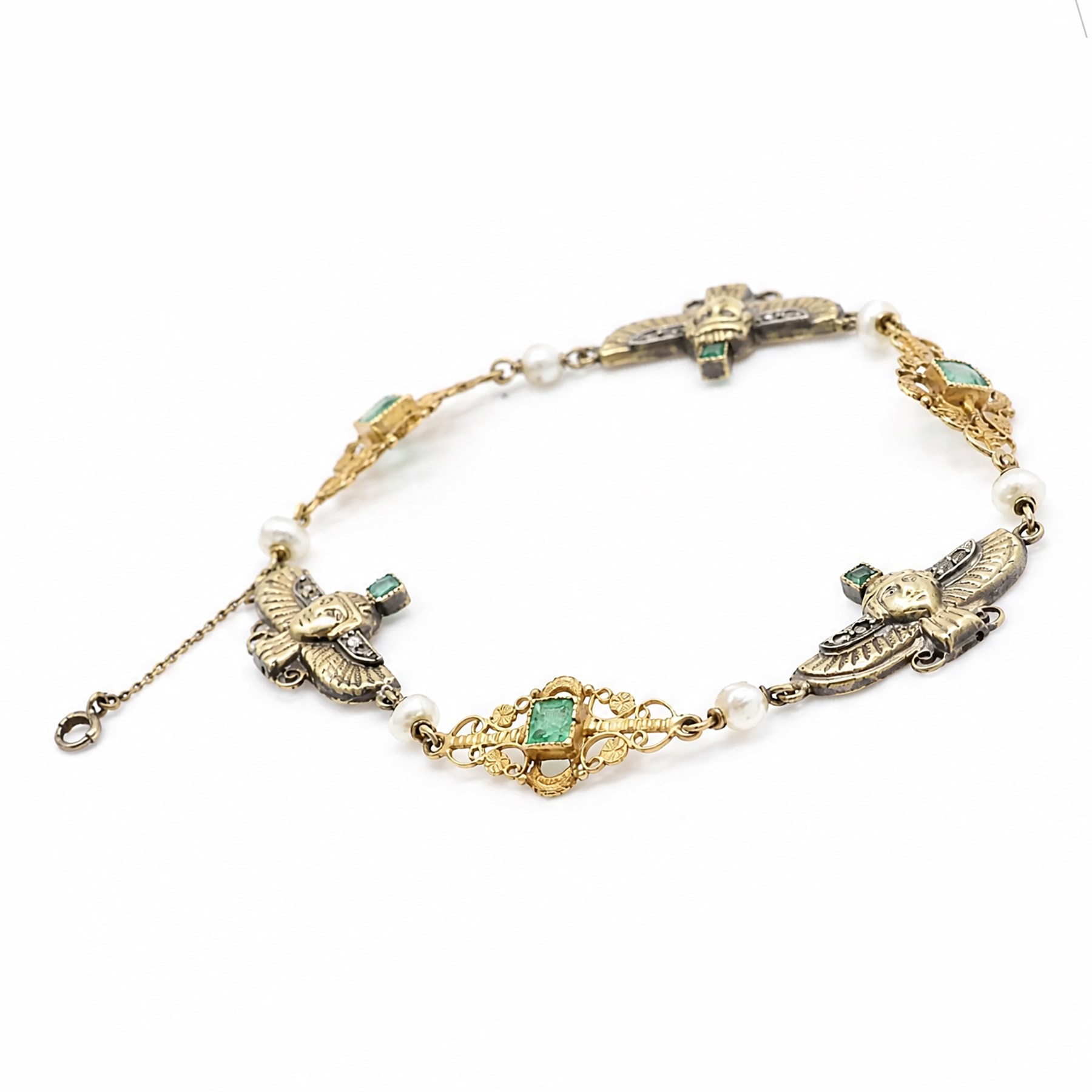 Early 20th century French 18ct gold Egyptian Revival bracelet, three winged sphinx motif panels, each set with a square cut emerald and four rose cut diamonds, spaced by six white / cream pearls and three scrolling openwork links, each centred with a square cut emerald, French assay marks