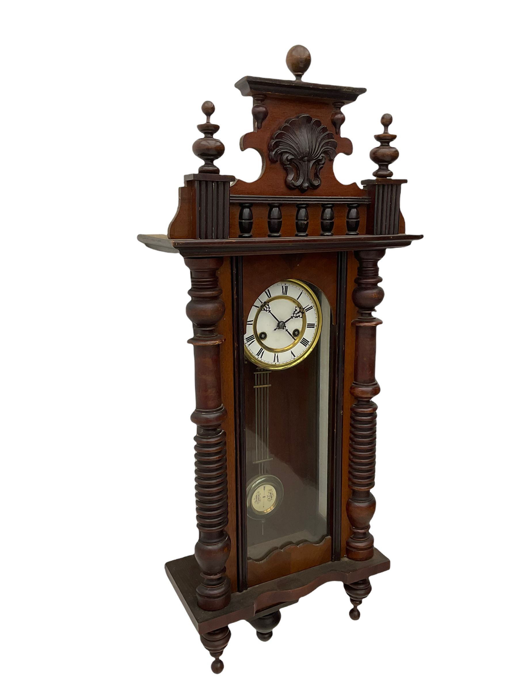 A  German spring driven wall clock c1900 within a glazed case with side panels and a full-length arched door and ornately carved pediment, turned finials and original pendant finials, with a 5' two-piece white enamel dial with roman numerals, minute markers and pierced steel gothic hands, with a visible gridiron pendulum with an R/A inscribed pressed brass bob, eight-day movement striking the hours and half hours on a coiled gong.  



