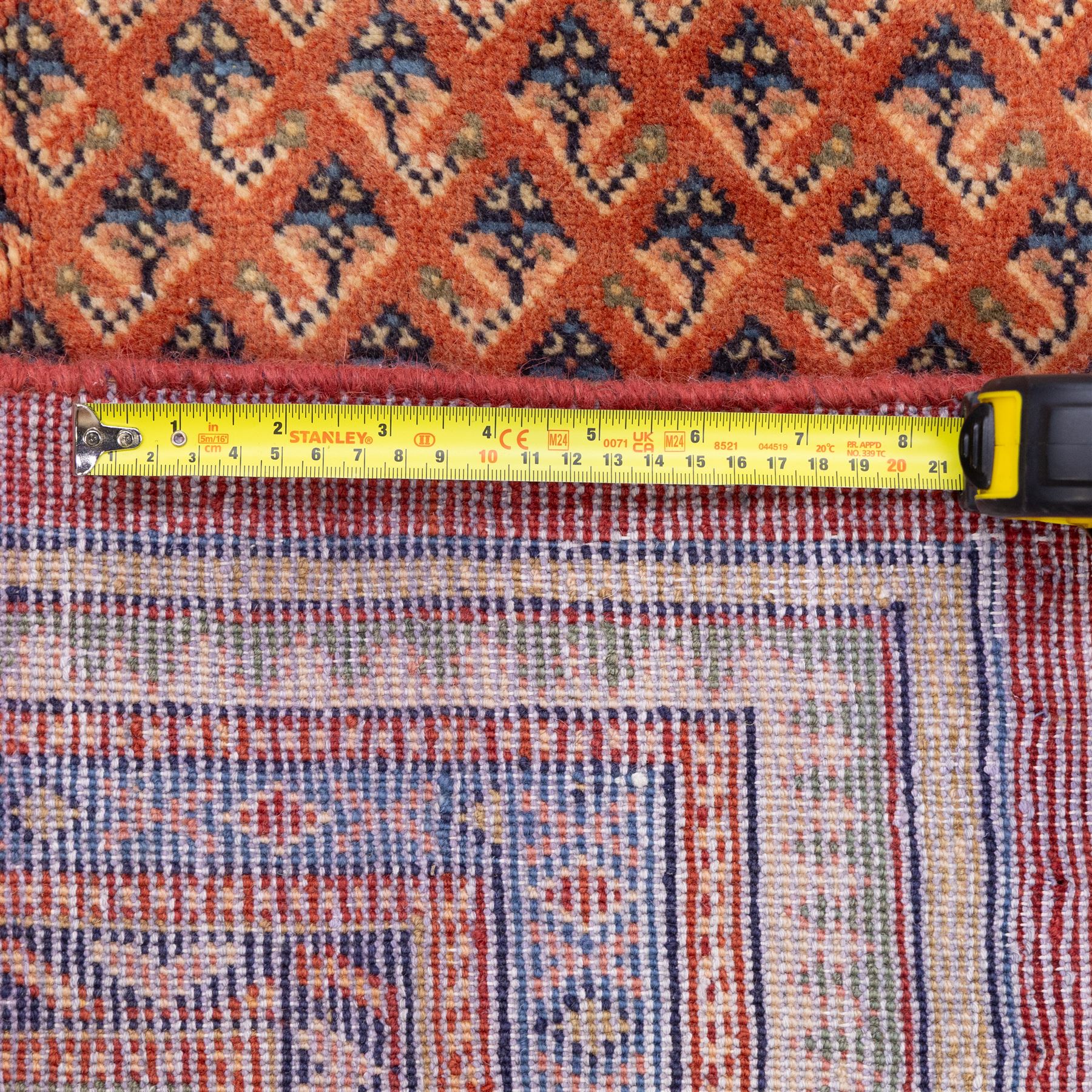 North West Persian Boteh-Mir hand-knotted rug, madder red field decorated with an all-over lattice of small boteh motifs and a central stepped lozenge medallion with repeating stylized boteh and geometric devices, spandrels similarly worked, with multiple narrow borders of floral and geometric bands, in tones of madder red, indigo blue, ivory, and soft green, with cotton fringe ends 