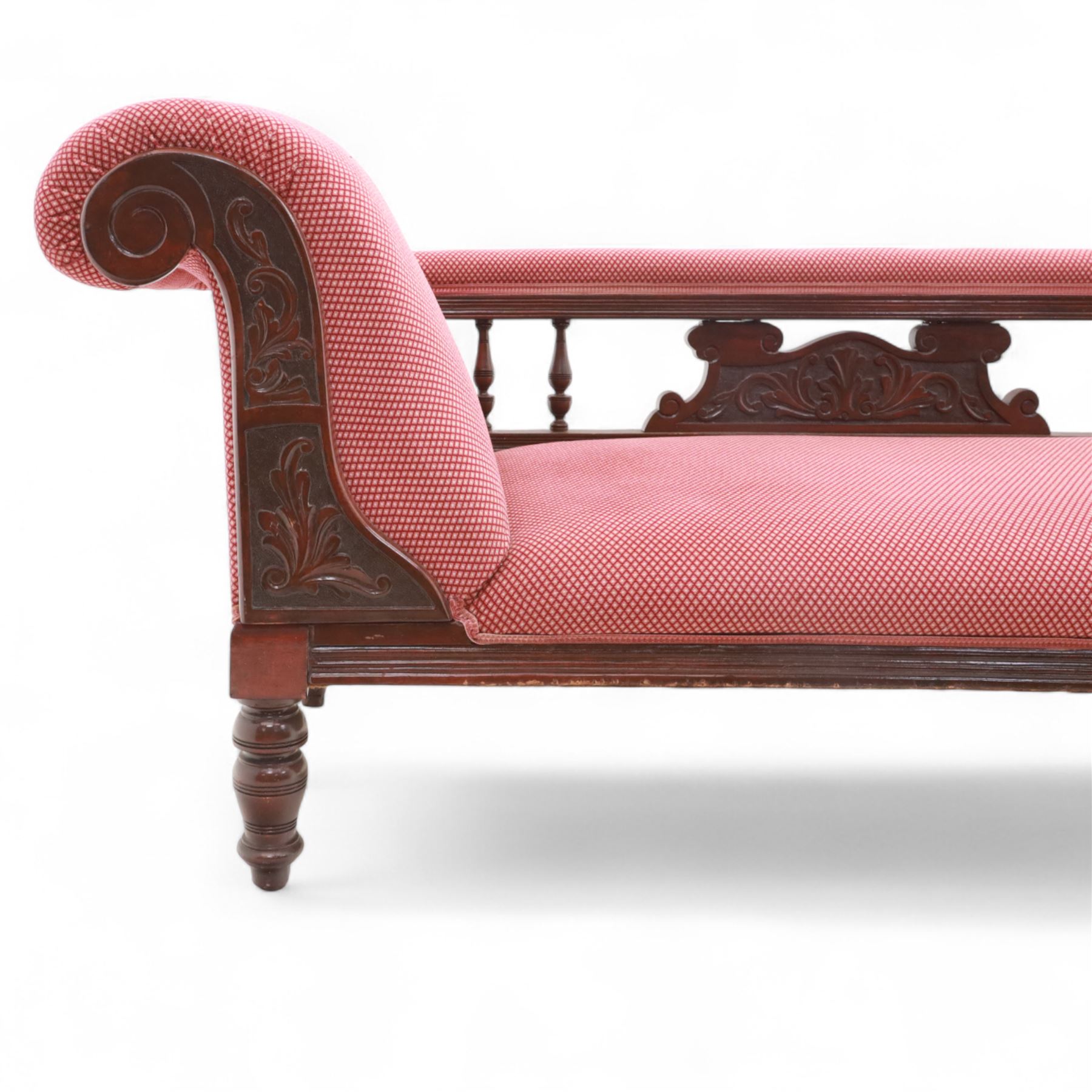 Late Victorian mahogany chaise longue, of scroll-ended form, upholstered in red diamond-patterned fabric with padded back and scroll-carved support, open arm with carved foliate and turned upright, raised on turned tapering legs 
