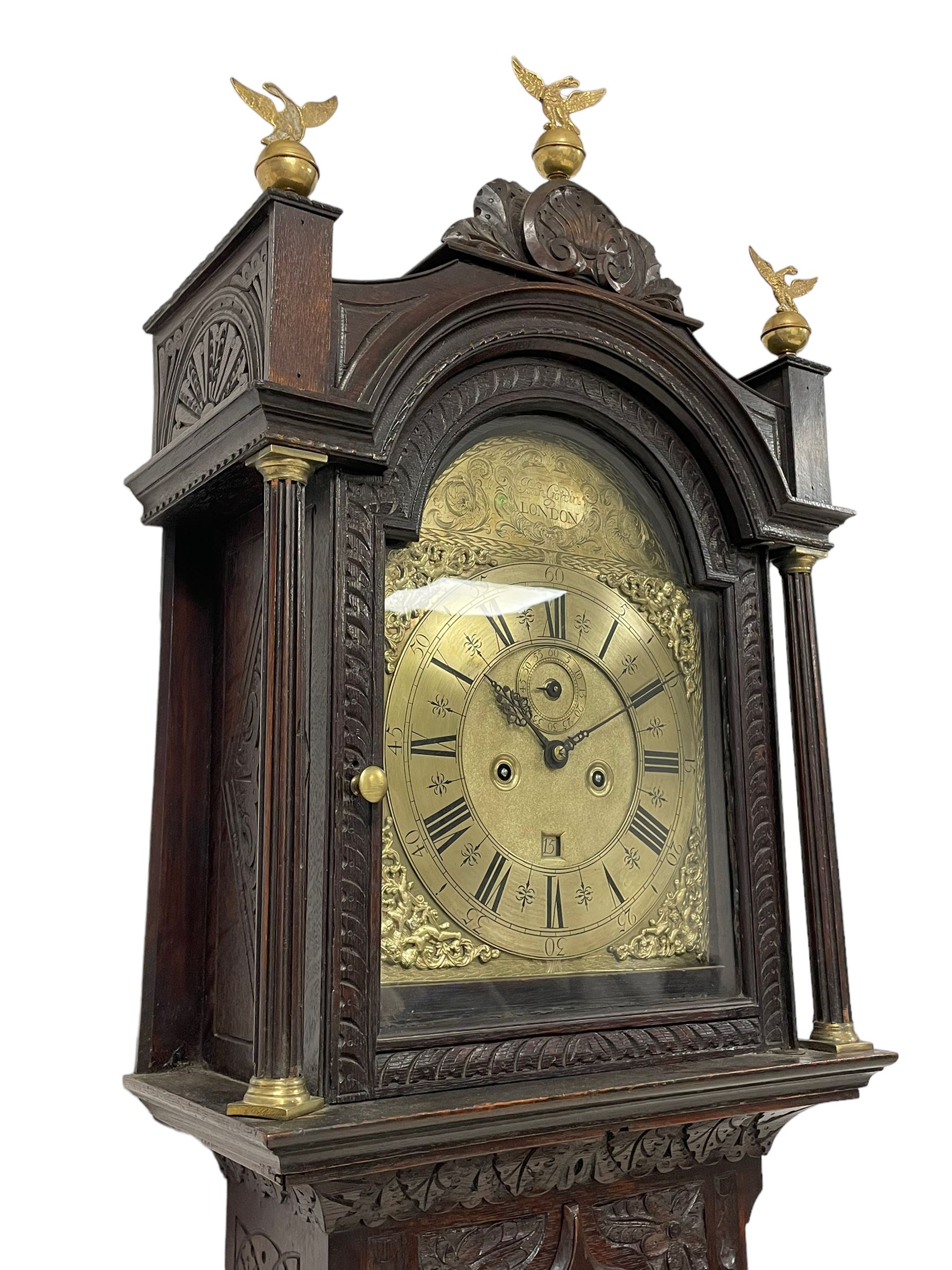 18th-century profusely carved oak longcase clock - with a pagoda pediment, upstands and carving, 
 break arch hood door flanked by reeded pilasters with brass capitals, trunk with canted corners and a spire topped door, square plinth with applied skirting, break arch brass dial with wheatsheaf engraving and cast cherub and crown spandrels, engraved break arch with the London clockmakers name John Gordin, silvered chapter ring with Roman numerals, five minute Arabic's, minute and quarter hour tracks, matted dial centre with ringed winding holes, square date aperture and seconds ring, dial pinned to a five pillar movement with inside countwheel striking, striking the hours on a cast bell. With weights and pendulum. John Gordin, is possibly a mis-spelling or phonetic spelling of John Gordon, of London, who worked from Ludgate Street in the parish of St. Gregory by St. Pauls. Apprenticed in 1689 and died in 1732 when his will was proven.

